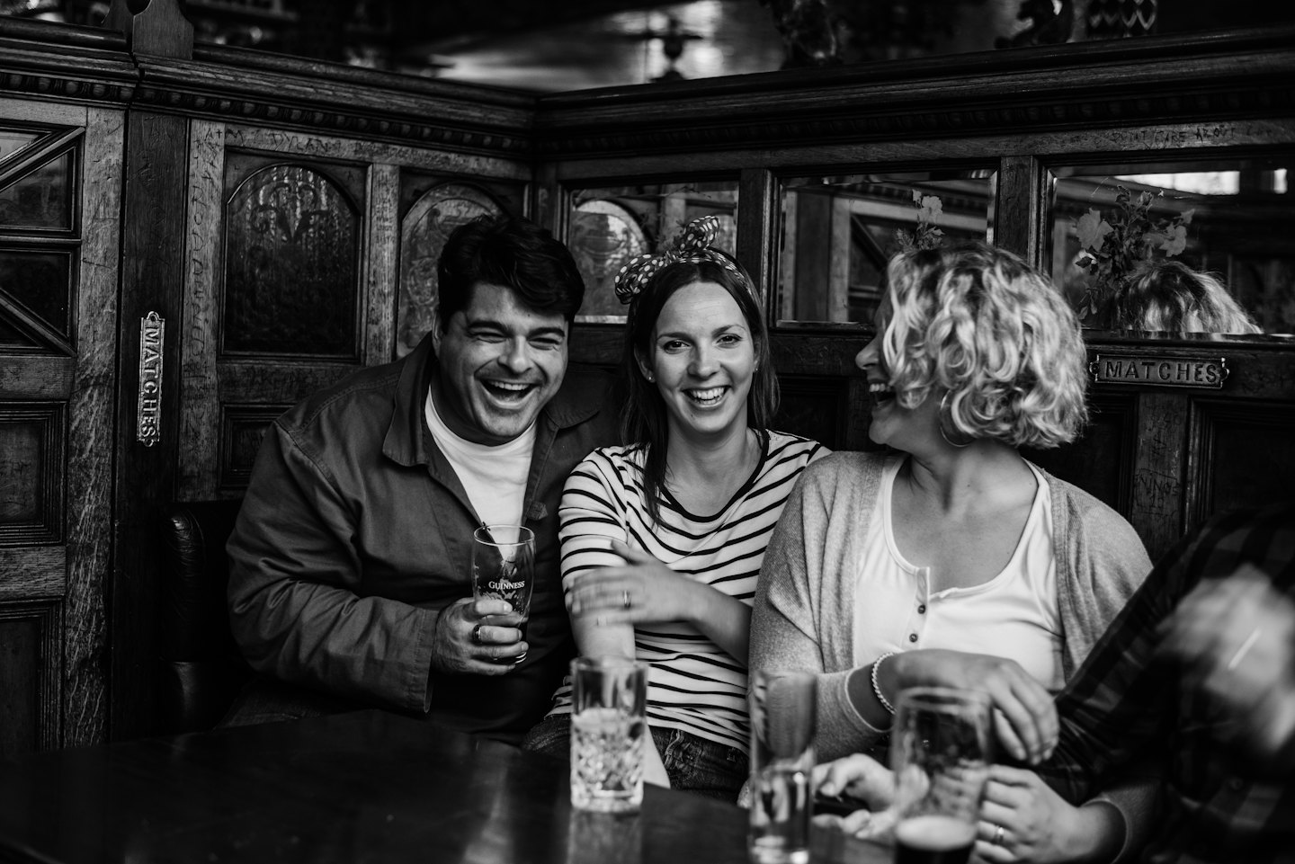 Three friends laughing together in a pub booth.