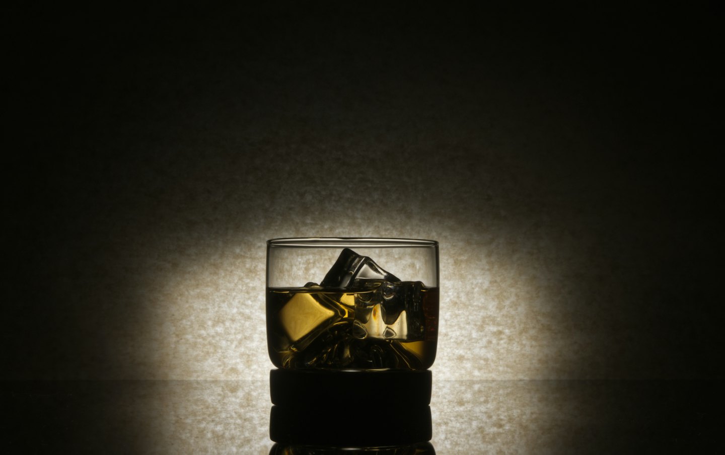 A glass of whiskey with ice sits on a dark surface.