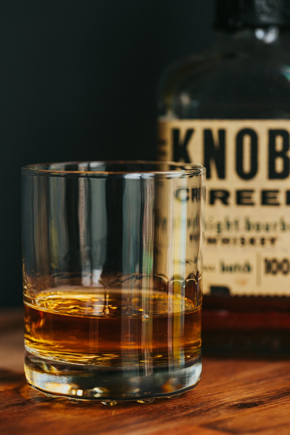 Glass of amber whiskey on a polished wooden surface.